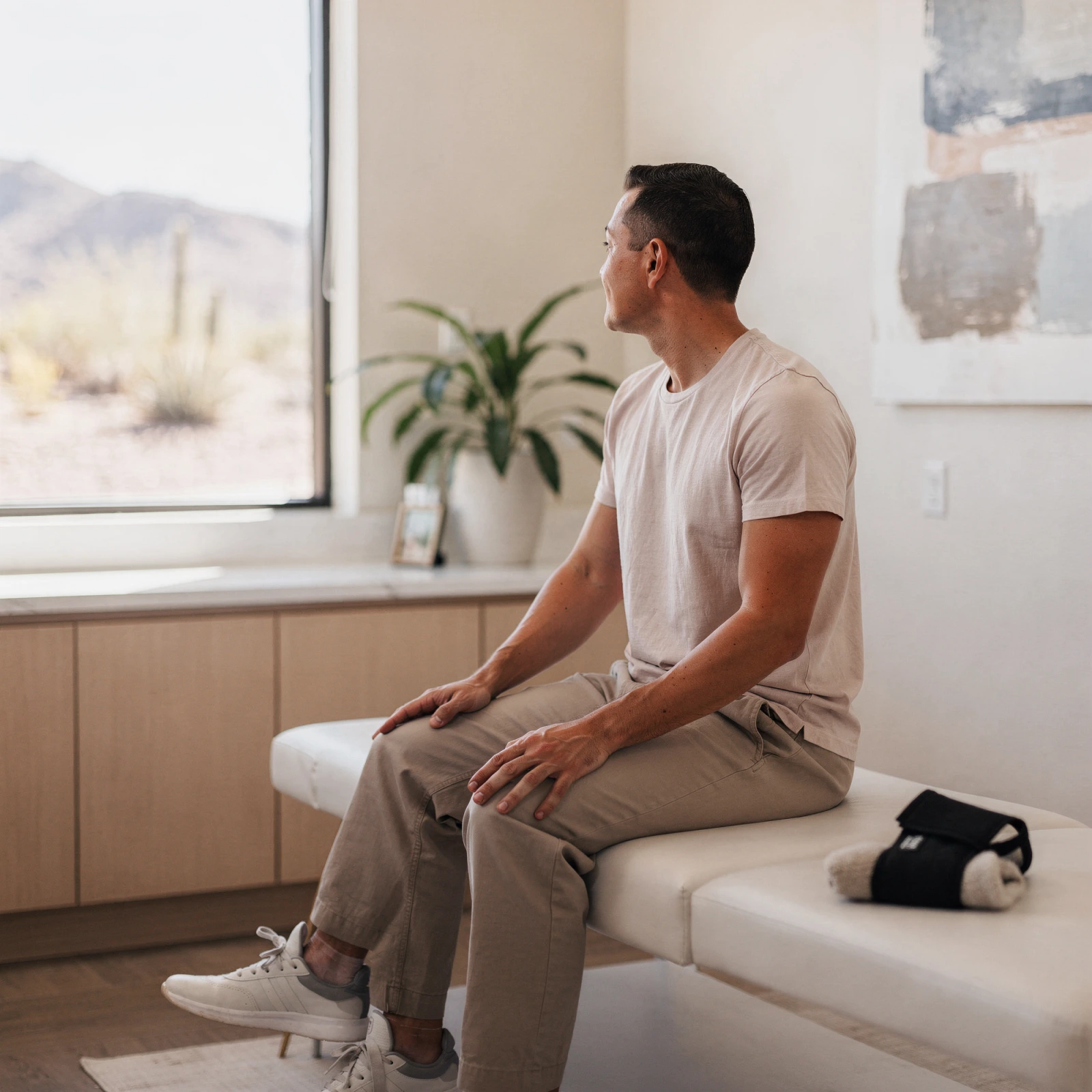 Patient sitting on examination table in a bright clinic room with desert mountain view